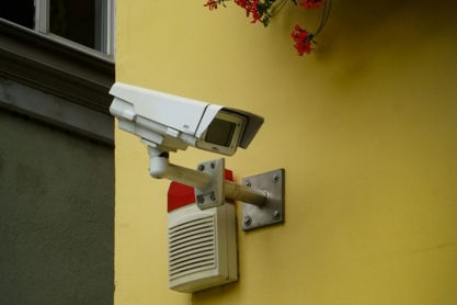 white and gray security camera mounted on yellow painted wall